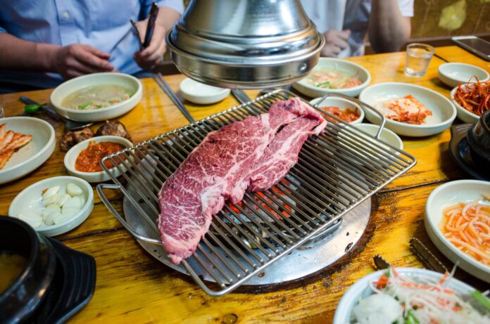 Carne pregătită pe un grătar coreean, cu garnituri în jurul mesei
